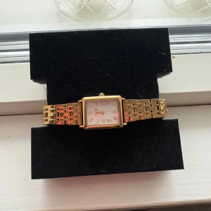 Guldfärgad klocka från Regal - Snygg guldfärgad klocka från Regal med fyrkantig urtavla och romerska siffror. Köpt på Plick så vet ej om den är helt ny, men de ser ut som de. Urtavlan är vit med guldiga detaljer. Inga repor eller något❣️