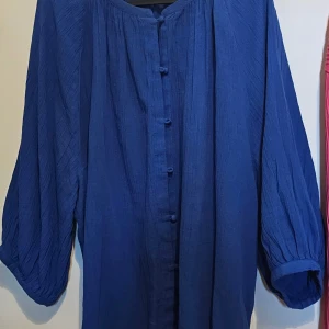 Blå skjorta med vida ärmar från H&M - Säljer en blå skjorta från H&M med avslappnad passform och vida, trekvartsärmar. Skjortan har knappar framtill och är tillverkad i ett lätt, strukturerat bomullstyg. Perfekt för dig som gillar en chill och luftig stil.