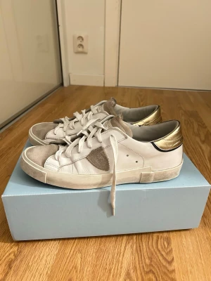 Philippe Model skor  - Vita Philippe Model sneakers med gulddetalj, använda fåtal gånger i somras, inga större slitningar (skorna har slitningar som design) Slulorna i skorna är Aldrig  använda och skolåda ingår💗 skriv för fler bilder eller om pris! Ny pris 3500kr