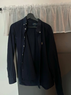 Mörkblå Ralph Lauren skjorta - Klassisk mörkblå skjorta från Polo Ralph Lauren med knappstängning och lång ärm. Skjortan har den ikoniska broderade loggan på bröstet och är tillverkad i mjuk bomull. Perfekt för en stilren och avslappnad look. Den passar storlek M/S och är använd sparsamt. Hör av er om ni har några frågor!🤩