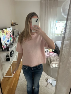 Ljusrosa stickad tröja med kort ärm - Söt ljusrosa stickad tröja med korta ärmar och avslappnad passform. Tröjan har rund halsringning och ribbade kanter vid ärmslut och nederkant. Perfekt för lager-på-lager och enkel att styla till jeans eller kjol.