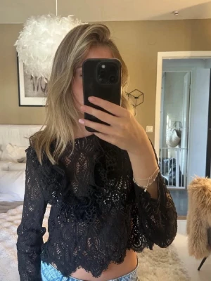 Svart spetsblus med volangdetaljer - Säljer en svart blus i spets med långa ärmar och volangdetaljer framtill. Perfekt Festtopp! 