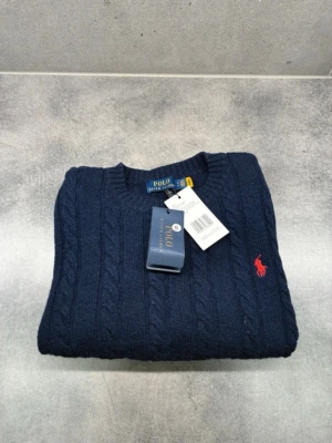 Mörkblå kabelstickad tröja Polo Ralph Lauren - Kabelstickad mörkblå tröja från Polo Ralph Lauren med rund halsringning och den klassiska röda logotypen broderad på bröstet. Tröjan har ribbade muddar och är perfekt för dig som gillar en tidlös och stilren look.