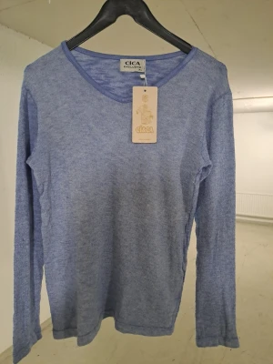 Ljusblå långärmad tröja Cica - Ljusblå långärmad tröja från Cica med enkel och stilren design. Tröjan har rund halsringning och är tillverkad i ett mjukt, tunt material som passar perfekt för lager på lager. En klassisk baströja som funkar till det mesta.