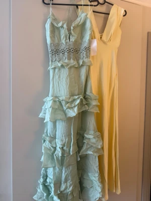 Ljusgrön volangklänning med spetsdetaljer - Säljer en ljusgrön långklänning med tunna axelband, volanger i flera lager och fina spetsdetaljer i midjan. Klänningen har en romantisk look och är perfekt för sommarens alla tillfällen. Materialet känns lätt och luftigt. Aldrig använd lappen kvar endast testad en gång 