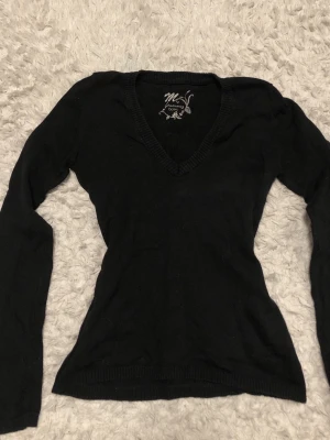 Svart V-ringad stickad tröja Stradivarius - Säljer en svart stickad tröja från Stradivarius Basic med V-ringning och långa ärmar. Tröjan har en figurnära passform och ribbade muddar vid ärmslut och nederkant. Perfekt att matcha med jeans eller kjol.