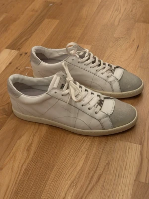 Corneliani Sneakers - Snygga vita sneakers från Corneliani med grå mockadetaljer på tån i strl 43 (passar 42 även). Skorna är kanske 4 år gamla och ganska oanvända som ni ser. De tar bara plats i garderoben. Har inte låda, dustbag eller snören tyvärr. 