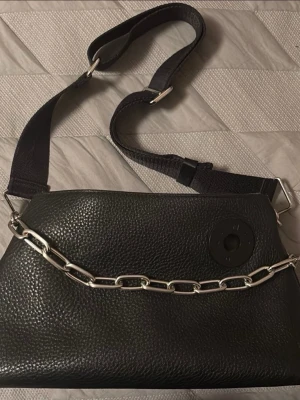 Svart axelväska från Bimba Y Lola - Bimba y Lola black bag  Svart väska med dragkedja och ett foder i en grön nyans. Två avtagbara remmar. En kortare kedja och en längre bred justerbar rem. Väskan har en etikett med texten ”BIMBA Y LOLA”. mått: 32,5 x 20 x 11 cm Lite spår av ålder på dragkedjan och spännena som fäster remmen. I övrigt väldigt fint skick  Titta gärna på mina andra annonser!