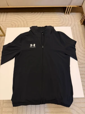 Svart vindjacka från Under Armour - Snygg svart vindjacka från Under Armour med hel dragkedja framtill och luva 