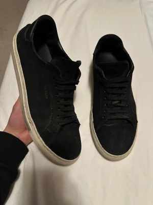 Axel Arigato - Svarta sneakers från Axel Arigato med klassisk låg profil och vit sula. Skorna har ovandel i mocka, rund tå och snörning framtill. Perfekta för en clean och stilren look.