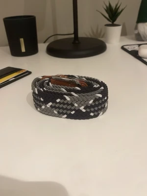 Flätat bälte  - Säljer en flätat bälte med vit, grå och svarta detaljer. Säljer för ett bra pris. 