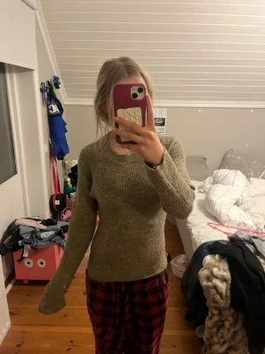 Olivgrön ribbstickad tröja - Säljer en olivgrön ribbstickad tröja med rund halsringning och långa ärmar. Tröjan har en figurnära passform och är perfekt för lager-på-lager. Materialet känns mjukt och stretchigt, vilket gör den skön att bära hela dagen. Omsydd! 