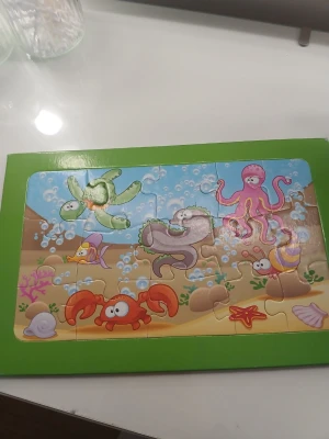 Färgglatt undervattenspussel i trä - Säljer ett färgglatt pussel med undervattenstema. Motivet visar tecknade havsdjur som sköldpadda, bläckfisk, krabba och fiskar. Pusslet har en grön ram och bitarna är stora och lätta att hantera, perfekt för yngre barn. (Kommer inte i orginalkartong)