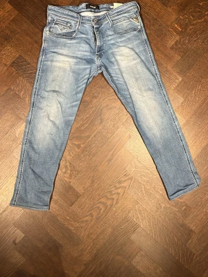 Replay anbass ljusblå  - Snygga ljusblå slim jeans från Replay med slitningar och klassiska fem fickor. Jeansen har en smal passform och är tillverkade i mjukt denimtyg med vita kontrastsömmar och Replay-logga på bakfickan. Passar dig som är 170
