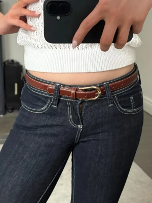 Brunt smalt bälte från Lindex - Snyggt brunt bälte från Lindex i smal modell med guldfärgat spänne. Tillverkat i konstläder och passar perfekt till jeans eller kjol för en clean och stilren look.