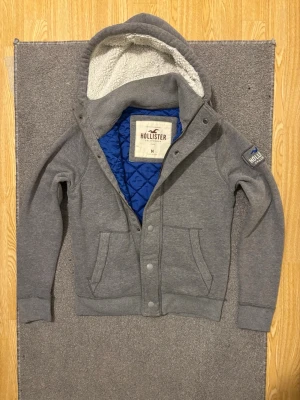 Vintage Hollister Hoodiejacka - Säljer denna as feta Hollister hoodiejackan med knappar & zip men även en mysig fodrad luva! | Storlek M men kan passa S! | Längd ≈ 65cm, Bredd armhåla - armhåla ≈55cm | Modell 175cm, 68kg | Hör av vid funderingar!