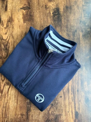 Sergio Tacchini Half Zip - Sergio Tacchini half zip i marinblått, storlek Small. Klassisk casuals-stil med rötter i brittisk fotbollskultur. Tidlös retrodesign med hög krage och dragkedja. Bekväm passform som funkar perfekt till jeans eller chinos. I bra skick utan hål eller fläckar.