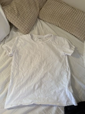 Vit basic t-shirt från 157 - En klassisk vit t-shirt från 157 med rund hals och korta ärmar. Tillverkad i mjuk bomull som känns skön mot huden. Perfekt att matcha med jeans eller shorts för en enkel och clean look.