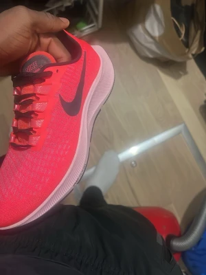 Nike rosa sneakers med svart swoosh - Snygga sneakers från Nike i en stark rosa färg med svart swoosh på sidan. Skorna har en låg profil, ventilerande mesh-överdel och klassisk snörning. Perfekta för dig som vill sticka ut med färg och sportig stil.