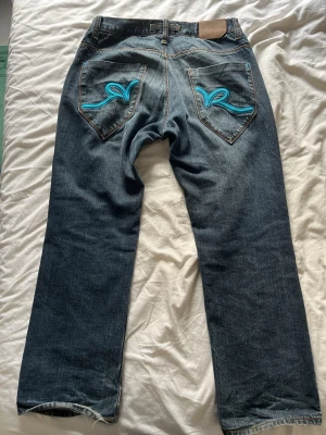 Vintage mörkblåa Rocawear jeans från 2000-talet - Säljer ett par vintage mörkblåa jeans från hip-hop legenden Jay-Z märke Rocawear från runt år 2000. På bakfickorna finns rocawear loggan i ljusblått. Storlek W36 L32. Mycket bra skick, lite slitage vid benöppningen. Skriv om du har några frågor eller vill diskutera priset!