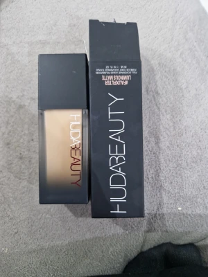Huda Beauty Faux Filter Foundation - Flytande foundation från Huda Beauty i nyansen Crème Brulee 150G. Ger full täckning med en luminous matt finish. Kommer i en stilren, fyrkantig glasflaska med svart lock och tillhörande svart kartong. Perfekt för dig som vill ha en jämn och flawless bas.