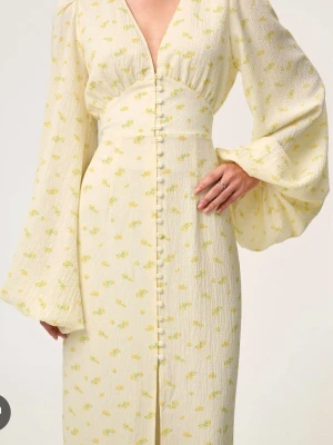 Ljusgul blommig långklänning - Romantisk ljusgul långklänning med små blommor, v-ringning och långa vida ärmar. Klänningen har knappar framtill och markerad midja för en feminin siluett. Perfekt för sommarens alla tillfällen. Änvänd ENDAST 2 gånger, köpt för 1800kr säljer för 1200