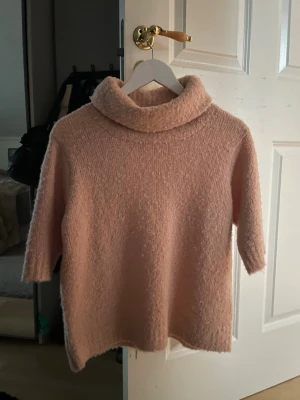 Ljusrosa stickad polotröja - Mysig ljusrosa stickad tröja med polokrage och trekvartsärmar. Tröjan har en lös passform och är tillverkad i ett fluffigt, mjukt material som känns skönt mot huden. Perfekt för lager-på-lager och chill dagar. Endast använd en gång