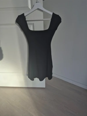 Svart kortärmad klänning med snörning - En svart, kortärmad klänning med djup urringning både fram och bak samt snygg snörningsdetalj i ryggen. Klänningen har en figurnära passform och är tillverkad i ett mjukt, stretchigt material som ger en bekväm känsla. Andvänd 1 ggr. Ord.pris: 799 kr