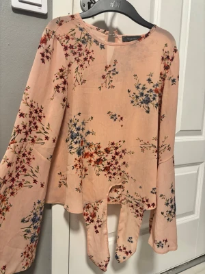 Blommig blus med vida ärmar H&M - Supersöt blus i ljusrosa med blommigt mönster i rött, blått och grönt. Blusen har rund halsringning, vida långärmar och asymmetrisk nederkant som ger en unik look. 