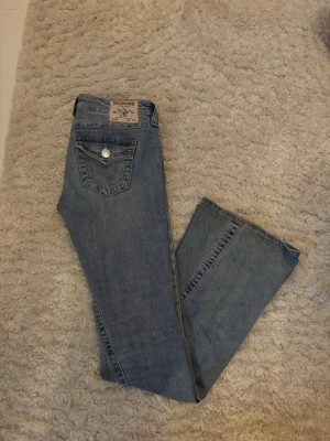 Ljusblå True Religion jeans - Säljer min tjejs jätte fina klassiska ljusblå jeans från True Religion med ikonisk fickdesign och silverfärgad knapp. Jeansen har raka ben och är tillverkade i mjukt denimtyg. Perfekta för en avslappnad och trendig look.