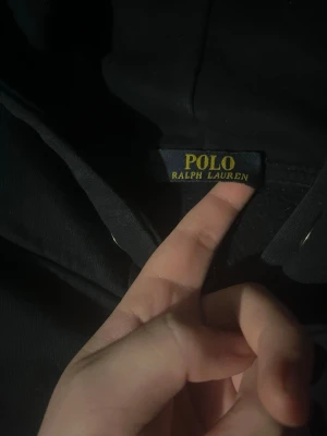 Svart hoodie från Polo Ralph Lauren - Säljer en svart hoodie från Polo Ralph Lauren med dragkedja framtill och klassisk huva med snören. Hoodien har fickor på magen och en broderad logga på bröstet. Perfekt för dig som gillar stilrena och tidlösa plagg.