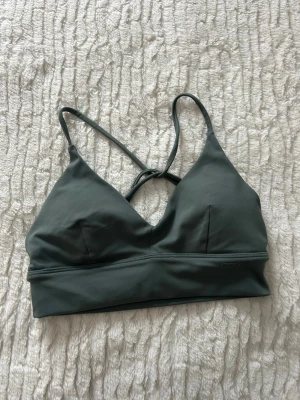 Ggrön sport-bh från Aim'n - Stilren grön sport-bh från Aim'n med smala korsade axelband i ryggen. Bh:n har en mjuk och stretchig känsla, utan bygel och med lätt vaddering. Perfekt för träning eller chill dagar. Endast använd en gång 