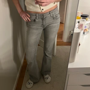 Grå bootcut jeans med låg midja - Snygga grå bootcut jeans med låg midja och klassiska fem fickor. Jeansen har en stilren look och är perfekta för dig som gillar en avslappnad men trendig stil. Passar till det mesta och är lätta att matcha med olika toppar. Använda fåtal gånger och inga defekter. Jag är 166 för referens. Är öppen för prisförslag 