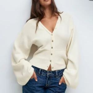 Vit kofta med ballongärmar - Trendig vit kofta med v-ringning och stora ballongärmar. Koftan har pärlemorknappar framtill och ribbade detaljer vid ärmslut och nederkant. Perfekt för dig som gillar en avslappnad men ändå stilren look. Knappt använd precks som ny!!😊