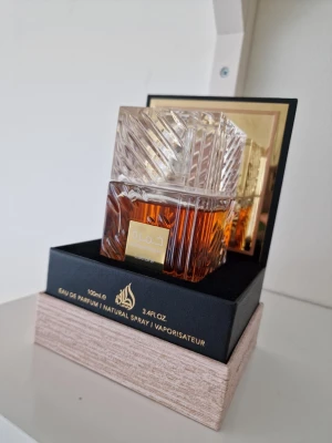 Khamrah Eau de Parfum 100ml - Khamrah Eau de Parfum från Lattafa i en elegant, fyrkantig glasflaska med ett detaljerat mönster och guldlabel. Doften kommer i en lyxig förpackning och har en varm bärnstensfärgad vätska. Perfekt för dig som gillar exklusiva och orientaliska parfymer. Använd endast 7, 8 ml max.