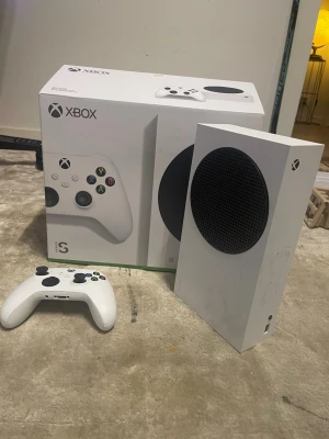 Xbox Series S spelkonsol med handkontroll - Säljer en Xbox Series S spelkonsol i vit färg med tillhörande vit trådlös handkontroll. Konsolen har en kompakt, rektangulär design med rund svart ventilationsyta på framsidan. Perfekt för gaming och digitala spelupplevelser. Spelat på den väldigt fåtal gånger, man får med HDMI, STRÖMKABEL och 1 Kontroll