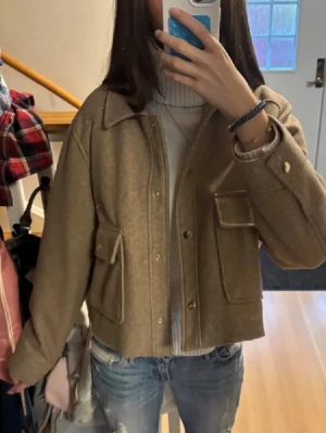 Beige cardiganjacka med fickor - Trendig beige cardiganjacka med stora fickor framtill och knappar. Jackan har en rak, boxig passform och klassisk krage. Perfekt att slänga över en polotröja för en chill och snygg look. INTE MINA BILDER. Storleken står XL men den passar bra till mig som har S/XS