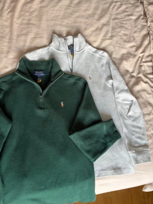 Två halvzip-tröjor från Polo Ralph Lauren - Säljer två snygga halvzip-tröjor från Polo Ralph Lauren. En i mörkgrönt och en i ljusgrått, båda med klassisk broderad logga på bröstet. Tröjorna har hög krage och är tillverkade i mjukt bomullsmaterial. Perfekta för en avslappnad men stilren look.    1 för 500, 2 för 900