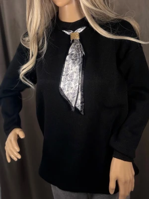 Vit paisleymönstrad halsduk med svart kant M-L☑️ - Snygg halsduk i vitt med svart paisleymönster och svart kant. Halsduken har en dekorativ guldfärgad brosch som håller ihop den framtill. Perfekt accessoar för att lyfta din outfit med en unik detalj.