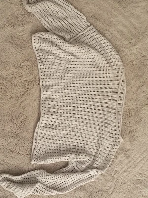 Vit nät övertröja oneshoulder  - Trendig vit stickad topp med oneshoulder-design. Toppen har ett luftigt, hålmönstrat material och är perfekt för att skapa en cool och avslappnad look. 