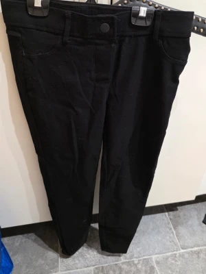 Svarta skinny jeans med normal hög midja - Snygga svarta skinny jeans med normal hög midja och klassisk femficksdesign. Jeansen har bälteshällor och knappstängning framtill. Materialet ser ut att vara stretchigt för en bekväm passform. Perfekta till alla typer av outfits!