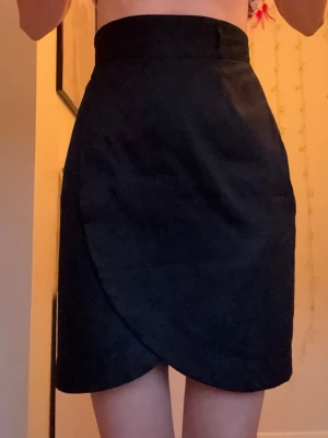 Svart omlottkjol H&M  - Stilren svart omlottkjol med hög midja. Kjolen har en enkel och elegant design med omlott-detalj framtill som ger en snygg siluett. Inte min från början så vet inte hur mycket använd den är, men den är i fint skick🥰Bara att höra av dig om du undrar nåt eller vill ha mått💕