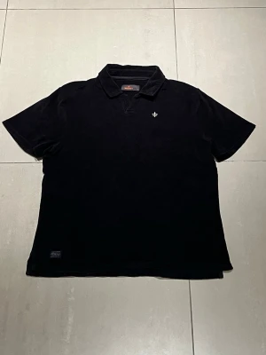 Svart frotté pikétröja från Morris. - Klassisk svart frotté pikétröja från Morris. Tröjan har en liten vit broderad logga på bröstet och är gjord i mjukt material som känns skönt mot huden. Perfekt för en clean och stilren look.