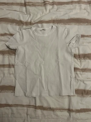 Vit basic t-shirt med kort ärm - En enkel vit t-shirt med rund hals och korta ärmar. Modellen är rak och har en klassisk passform, perfekt att matcha med allt. Materialet känns som mjuk bomull och t-shirten har inga tryck eller loggor.