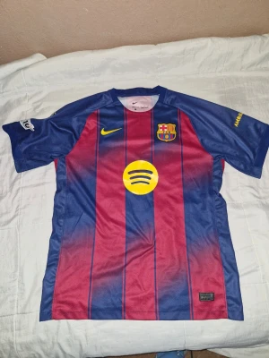 FC Barcelona 25/26 tröja - Säljer en FC Barcelona matchtröja från Nike i blått och vinrött med gula detaljer. Tröjan har klubbmärke, Spotify-logga och tryck med Rashford 14 på ryggen. Materialet är lätt och andas, perfekt för fotbollsträning eller match. 