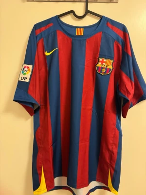 FC Barcelona matchtröja Nike S - Säljer en klassisk FC Barcelona matchtröja från Nike i storlek S. Tröjan har blå och röda vertikala ränder, klubbmärke på bröstet, gul Nike-logga och LFP-märke på ärmen. Tillverkad i polyester, perfekt för fotboll eller som supporterplagg.