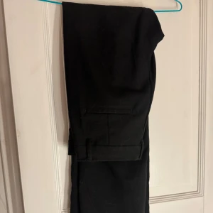 Svarta kostymbyxor från Monki - Snygga svarta kostymbyxor från Monki i storlek 38. Midwaist, klassisk rak modell med fickliknande detaljer både fram och bak. Säljer då de inte passar mig och de är knappt använda.