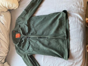 Grön overshirt från Superdry - Snygg militärgrön overshirt från Superdry Rookie Edition med klassisk passform. Skjortan har två bröstfickor med lock, dragkedja och knappar framtill samt patch på ena ärmen. Perfekt lager-på-lager-plagg med coola detaljer. Perfekt till höst, vår och sommar!