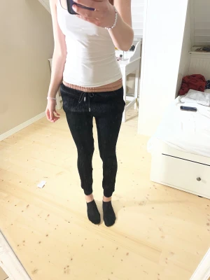 Svarta mjukisbyxor från Zara - Svarta mjukisbyxor från Zara med ribbad, beige midja och snörning. Byxorna har smal passform och muddar vid bensluten. Perfekta för chill eller häng med kompisar. Materialet är mjukt och bekvämt, midjan är elastisk för extra komfort. Modellen är 172cm lång.