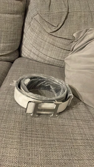 Vitt skärp med silverfärgat H-spänne - Snyggt vitt bälte med ett stort, stilrent H-format spänne i silver. Bältet är gjort i skinn och har en clean look som passar till många outfits. Perfekt accessoar för dig som vill sticka ut med en modern och fräsch detalj.